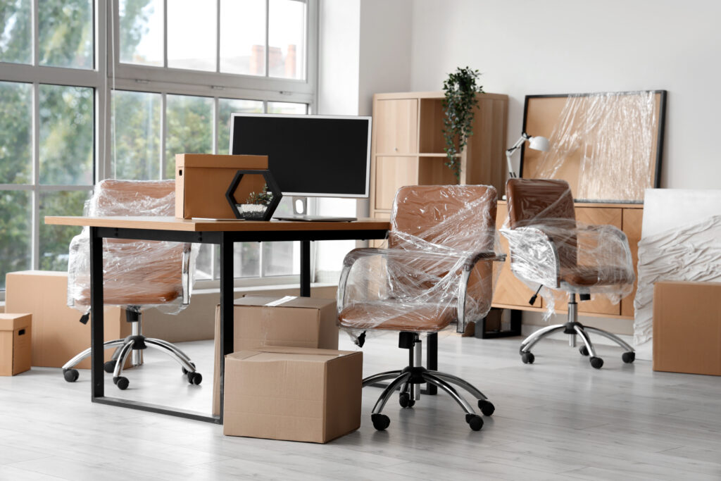 Büroumzug mit verpackten Bürostühlen, Schreibtisch und Kartons in einem modernen Büro – professioneller Firmenumzug mit Montage-Service.